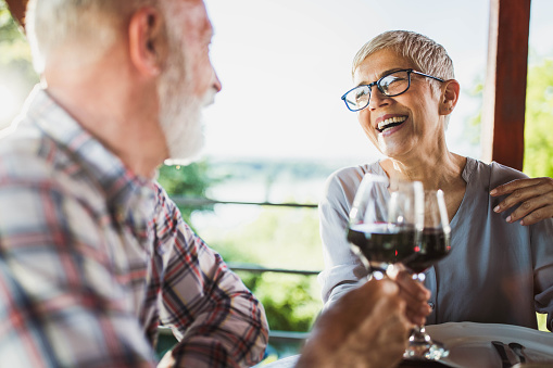 Happy mature couple communicating while toasting with red wine during their meal on a balcony.