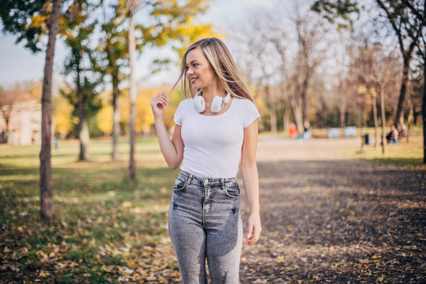 Pretty young woman is walking in the park and listening to music.