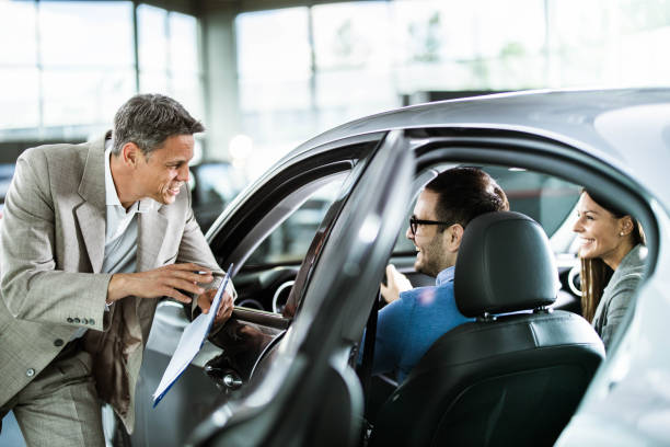 happy car salesperson talking to young couple in a showroom. - car test drive car rental women imagens e fotografias de stock