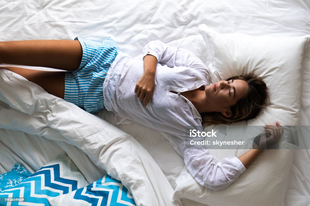 Above view of relaxed woman sleeping in bed. High angle view of young woman taking a nap in a bed. Adult Stock Photo