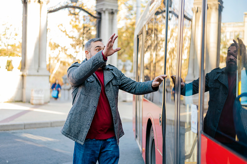 Handsome Bearded Man is Chasing the Public Bus. Mature Man in Jacket and Jeans is Waving to Bus Driver to Stop the Bus.