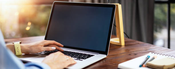 Mockup image of a woman using laptop with blank screen on wooden table stock photo