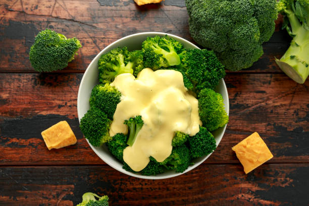 Broccoli with cheese sauce in white bowl on wooden table