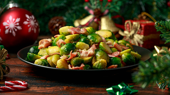 Christmas Brussel Sprouts and Bacon with decoration, gifts, green tree branch on wooden rustic table.