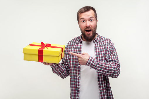 Portrait of excited wondered bearded man in casual plaid shirt pointing at wrapped present box and showing surprise on face, amazed by holiday gift. indoor studio shot isolated on white background