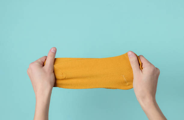 istock Female hands holding orange socks on a blue background. Top view 1192662814
