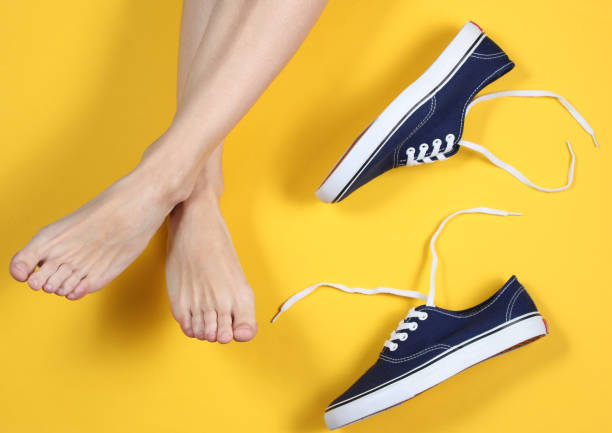 istock Women's bare feet on a yellow background with sneakers. Top view 1192663773