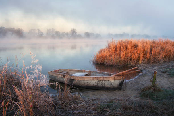 Misty autumn landscape. Plain quiet river and boat ashore.