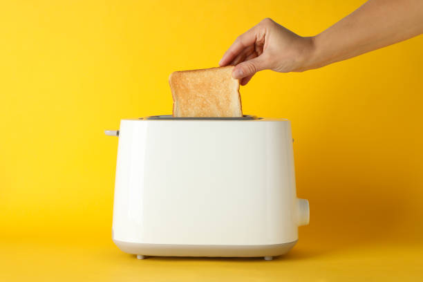 istock Female hand puts bread in a toaster on yellow background, space for text 1192667512