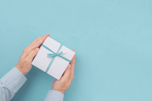 istock Hands holding Gift box with blue bow with copy space in craft paper over blue background. Top view, flat lay 1192669184