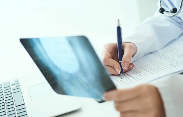 Close up of female doctor holding x-ray or roentgen image and making notes in medical form. Side view. Female doctor holding x-ray or roentgen image and making notes in medical form roentgen stock pictures, royalty-free photos & images