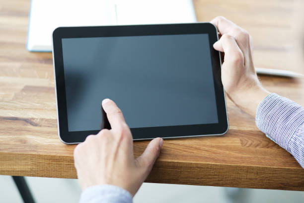 istock Man's hands holding blank tablet device over a wooden work space table. 1192671505