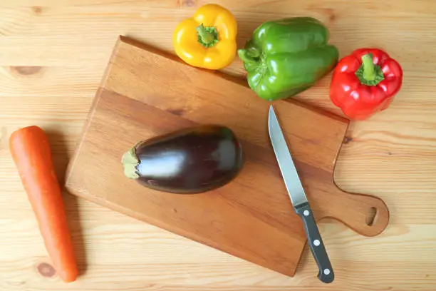 Top view of eggplant on cutting board with knife and bell-peppers
