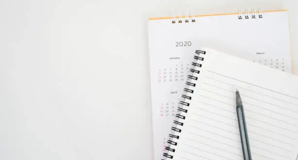 Photo of close up top view on  white calendar schedule background with pen and notebook to make appointment meeting or manage timetable each day for planning work in new year 2020 resolution concept