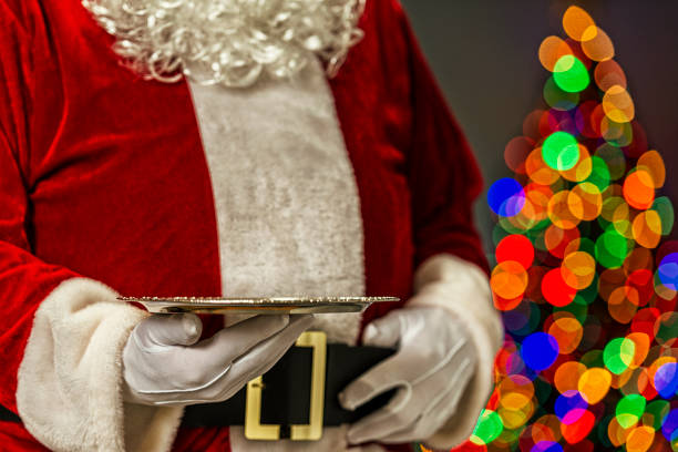 Santa Claus holding an empty silver platter and bokeh from Christmas tree in the background Santa Claus holding a blank empty Silver Platter and in the background the bokeh of multi-colored Christmas tree lights silver platter stock pictures, royalty-free photos & images