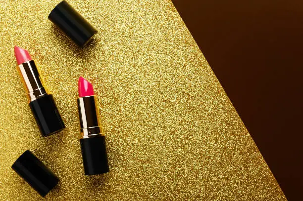 Lipsticks top view on golden glittery background. Fashionable red lipgloss on shimmering sequin flat lay backdrop. Creative luxury cosmetics, makeup accessory advertisement with text space.