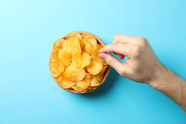 istock Hand holds potato chips on blue background, space for text. Top view 1192704725