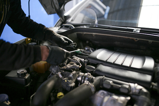 Auto mechanic working on a car engine in repair shop.