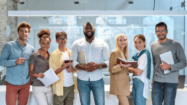 Dream work. Portrait of young and successful co-workers in casual wear smiling at camera while standing in working space Portrait of young and successful co-workers in casual wear smiling at camera while standing in working space. Teamwork concept. Collaboration race office stock pictures, royalty-free photos & images