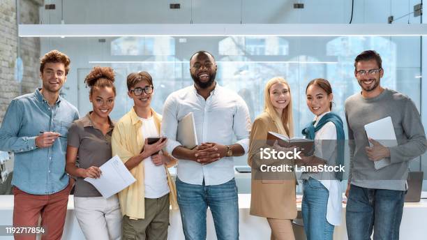 Dream Work Portrait Of Young And Successful Coworkers In Casual Wear Smiling At Camera While Standing In Working Space Stock Photo - Download Image Now