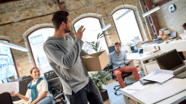 follow your dreams, quit your job. handsome man in casual wear holding box with personal things and saying good bye to his ex-colleagues while leaving modern office - quitting imagens e fotografias de stock