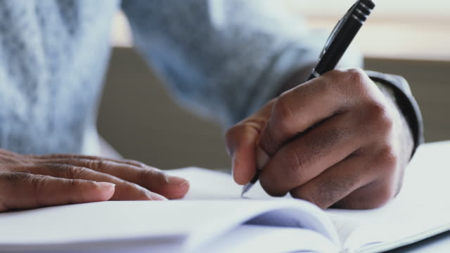 African left-handed businessman holding pen writing in organizer, close up