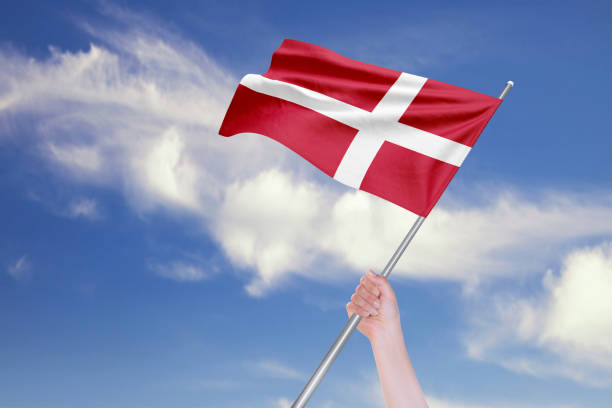 istock Female Hand is Waving Danish Flag Against Blue Sky with Clouds 1192720472