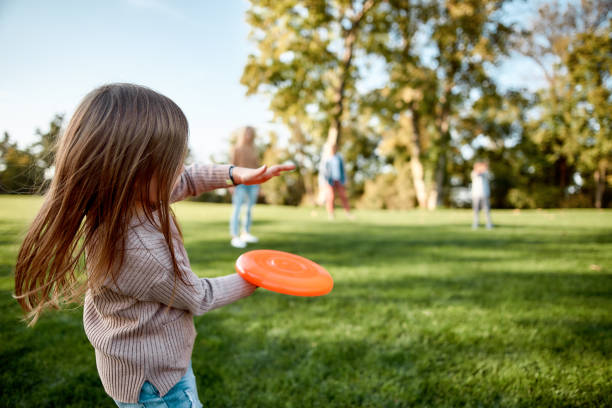 faire des souvenirs, briser la distance. petite fille jouant le frisbee avec sa famille dans le stationnement un jour ensoleillé - disque volant photos et images de collection