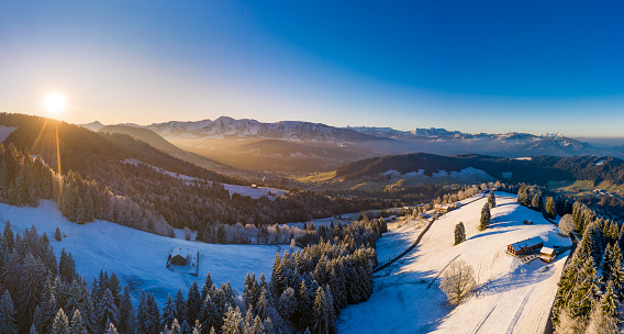 Bird's-eye view of a sunrise at a cold winter morning in the Bregenzerwald region in Vorarlberg. A frozen forest in the foreground and the small village Krumbach in the background.