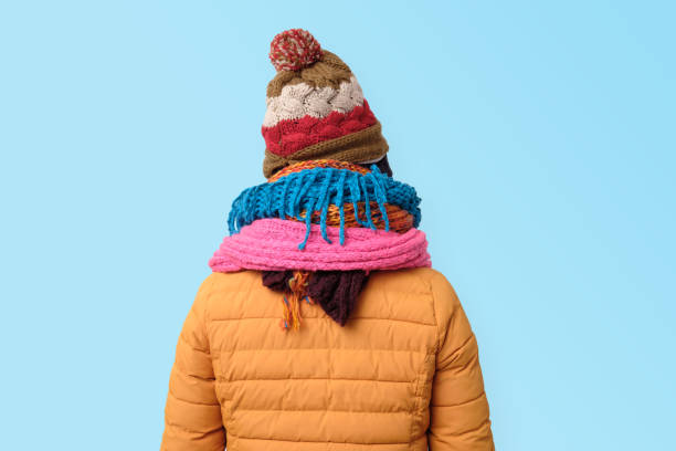 Handsome caucasian funny man hiding face in several hats and scarfs. Rear view. Winter fashion.