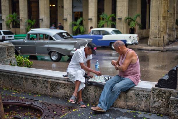Havana, Cuba - June 04, 2015: Two men playing chess on a rainy day, after the rain passed, on the edge of the road near the street with cars, in the middle of the day, in Havana, Cuba.