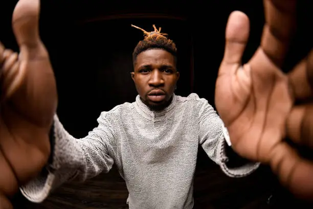 Fish-eye photo black man with blonde dreadlocks posing holding camera looking at lens in the black background in the studio