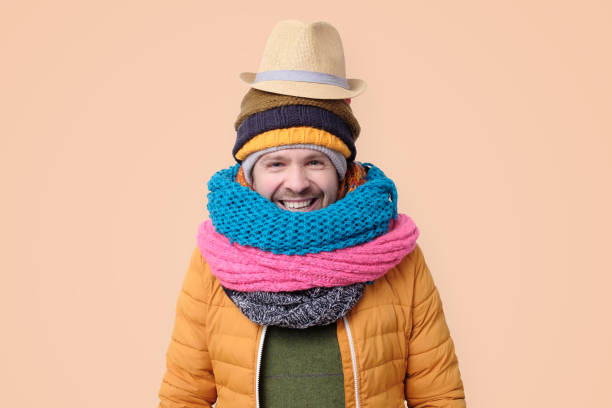 Funny man in several hats and scarfs with summer hat ready for holidays. Winter fashion.