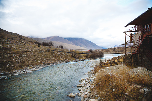A sinuous mountain river with clear water flows under a bridge in the countryside against the backdrop of the mountains in Upper Balkaria.
