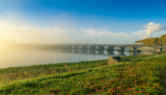 Bridge leading over the river Loire at Beaugency, France. The sun is just rising and the mist is still hanging over the bridge. The route is D925 and the city is located near Orleans, and south of Paris