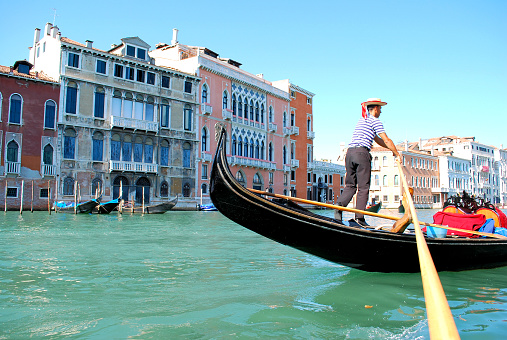 This photograph (captured in August of 2008) shows a traditional Venetian gondola being operated by a gondolier (boat operator), who is maneuvering across the canal by rowing with two long oars.  The gondola rides are an immensely popular tourist activity in Venice, Italy, and for most visitors it's a must do on their vacation's itinerary.  In 2019, most gondola rides in Venice were priced around 80 to 150 euros, along with ride times averaging between 40 to 60 minutes.