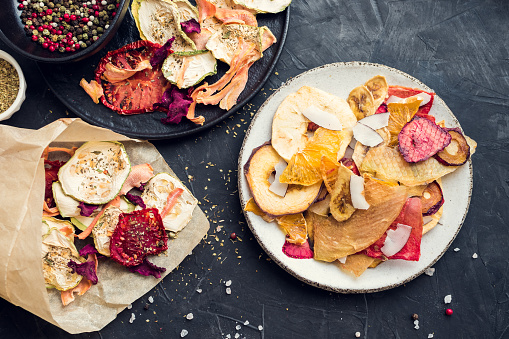 Healthy homemade fruit and vegetable chips on dark background. Organic diet food. The vegan diet. Dried vegetables. Vegetarian plant based snack concept. Top view.