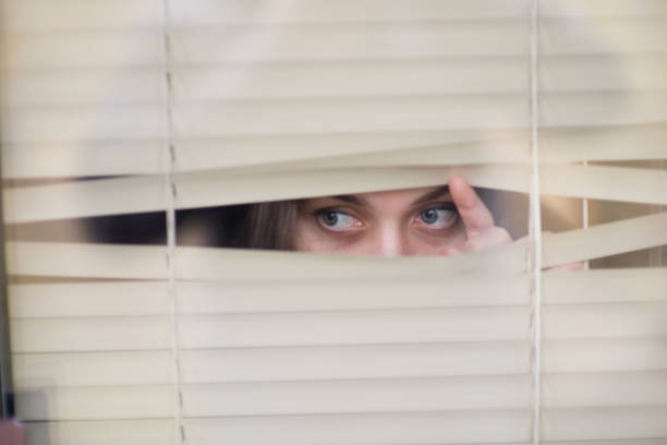 istock a sickly-looking woman looks through the window blinds 1192760128