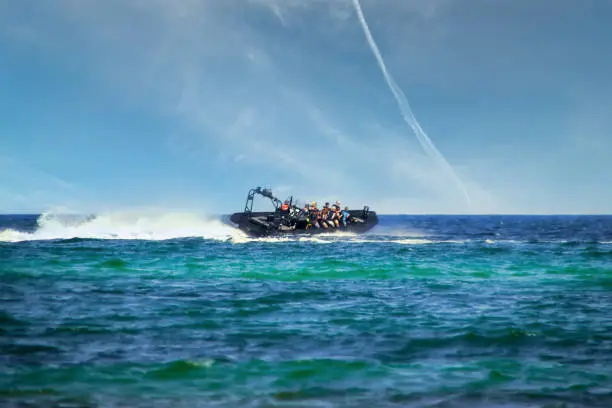 a speedboat with people on board lies in the bend in the turquoise blue water and lets a fountain spray up behind him