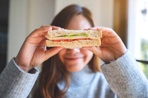 woman holding a piece of whole wheat sandwich cover her eyes A smiley beautiful woman holding a piece of whole wheat sandwich cover her eyes sandwich healthy lifestyle healthy eating bread stock pictures, royalty-free photos & images