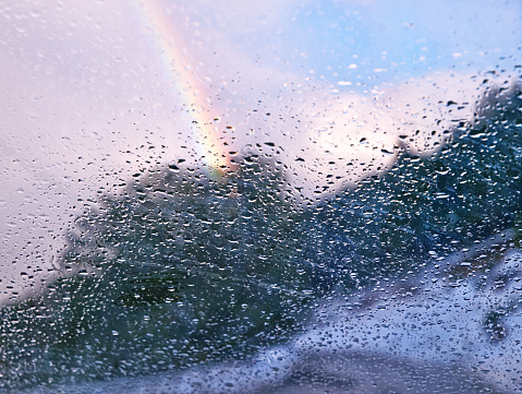 Rainbow behind car window glass with rain drops. After rain concept. Selective focus on window glass.