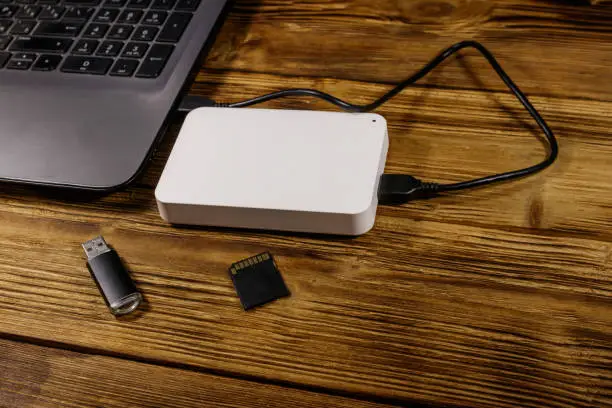 Photo of External HDD connected to laptop computer, SD memory card and USB flash drive on a wooden desk. Concept of data storage