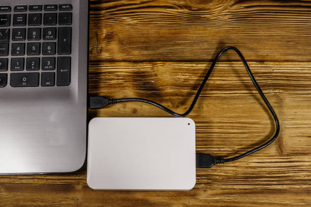 istock External HDD connected to laptop computer on a wooden desk. Top view. Concept of data storage 1192802315