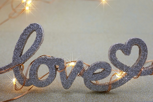 Love concept. Valentine's Day. The word love and a garland on a gold glitter background.Romantic twinkle background.
