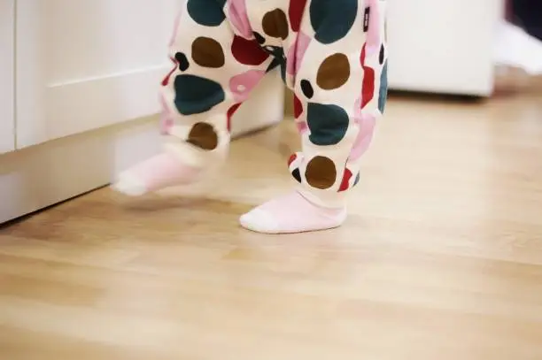 Photo of 1 year old baby walking on laminated wooden floor in a bedroom. toddler walking wobbly in exercise practice. children development and family caring concept.