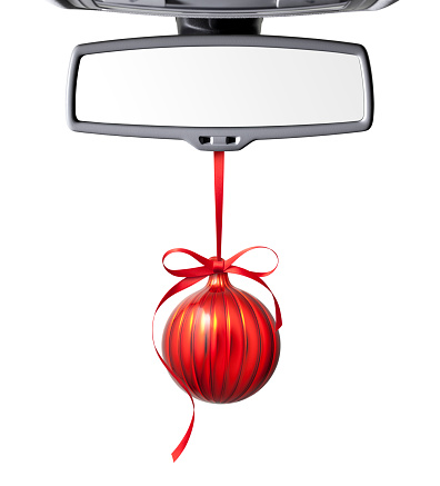 Red Christmas ball hanging from rear view mirror of car on white background.
