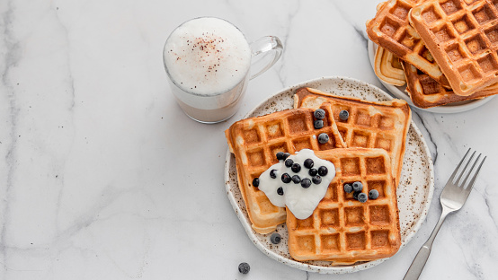 Delicious homemade baked belgian waffles with greek yogurt, blueberries and cappuccino on white marble background. Perfect breakfast with copy space for text or design. Top view or flat lay.