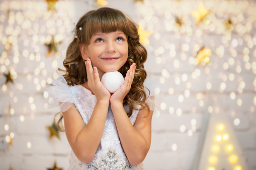 Beautiful child with a Christmas ball. Little model girl in a white dress. Smart girl