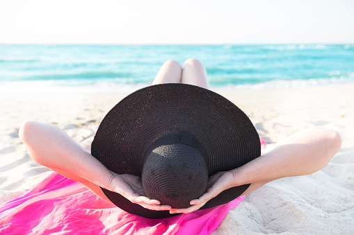 Big beach hat female figure on a background of the sea. Summer vacation on the beach.Woman in a hat sunbathes