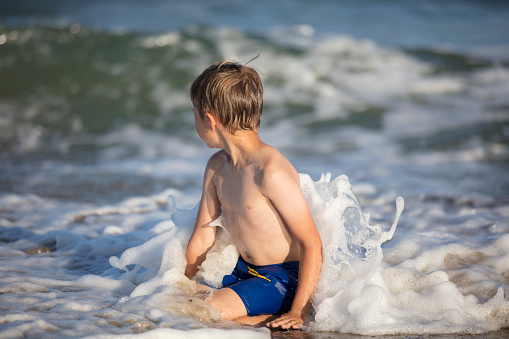 Joyful boy near the sea plays with the waves. Child resting on the beach